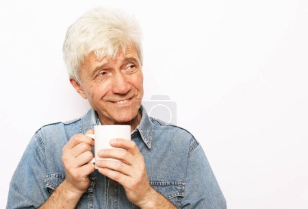 Foto de Alegre sonriente anciano sosteniendo una taza de café y sonriendo sobre fondo blanco - Imagen libre de derechos