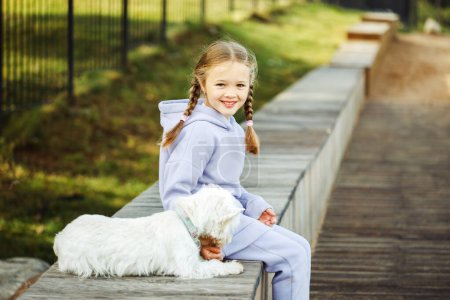 Téléchargez les photos : Fille blonde de sept ans jouant avec son chiot blanc dans le parc d'automne - en image libre de droit
