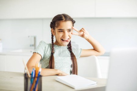 Photo for Schoolgirl with pigtails sitting at home at laptop and doing homework - Royalty Free Image