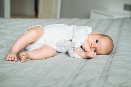 Photo for Newborn baby girl in white overalls lies on a blanket. Infancy, people and childhood concept. - Royalty Free Image