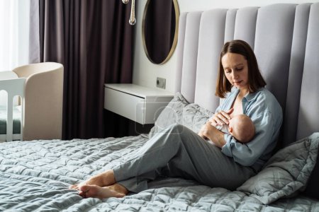 Téléchargez les photos : Portrait à la maison d'un nouveau-né avec une jeune mère sur le lit. L'amour d'une mère et d'un bébé. Famille dans la maison. - en image libre de droit