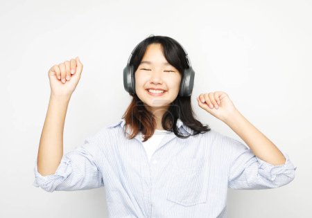 Téléchargez les photos : Jolie adolescente asiatique souriante écoute de la musique sur écouteurs sur fond blanc. Gros plan portrait. - en image libre de droit