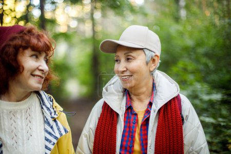 Zwei fröhliche Rentnerinnen plaudern und lachen im Herbstpark.