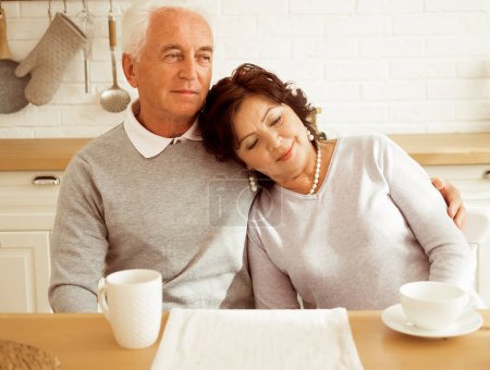 Foto de Happy elderly couple drinking coffee in the morning in the kitchen. - Imagen libre de derechos