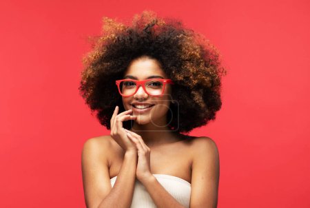 Photo for Happy young Afro woman wearing eyeglasses smiling, has good mood isolated on studio red background. - Royalty Free Image