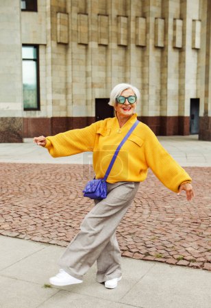 Foto de Una alegre anciana con un suéter amarillo se relaja en la calle en un día de verano. Concepto de estilo de vida y personas. - Imagen libre de derechos