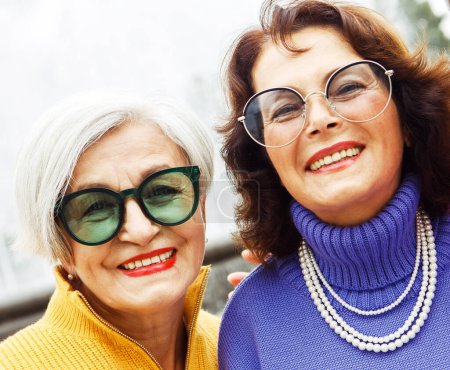 Photo for Two happy cheerful pensioner female friends in bright sweaters and sunglasses walk together. Lifestyle and people concept. - Royalty Free Image