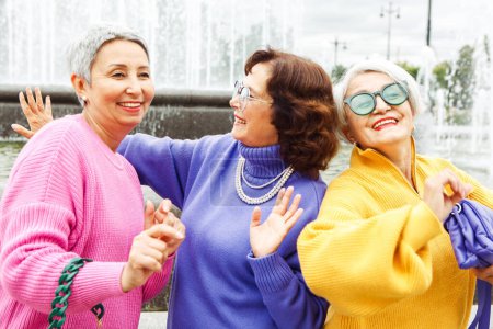 Photo for Three happy cheerful pensioner female friends in bright sweaters and sunglasses walk together. Lifestyle and people concept. - Royalty Free Image
