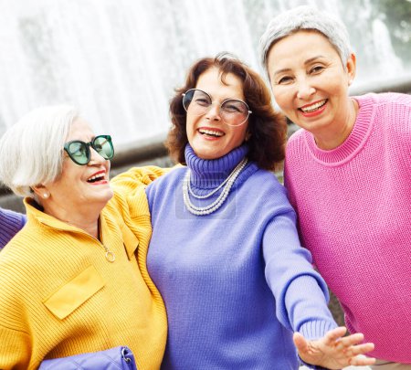 Foto de Tres felices jubiladas alegres amigas en suéteres brillantes y gafas de sol caminan juntas. Concepto de estilo de vida y personas. - Imagen libre de derechos