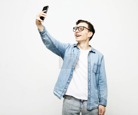 Foto de Retrato de un joven guapo tomando una selfie, sosteniendo un teléfono sobre fondo blanco. - Imagen libre de derechos