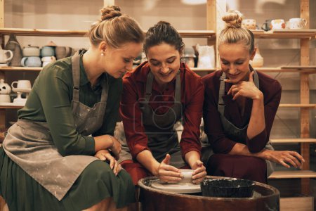 Téléchargez les photos : Une entreprise de trois jolies jeunes amies fait des tasses en céramique dans un atelier de poterie. - en image libre de droit