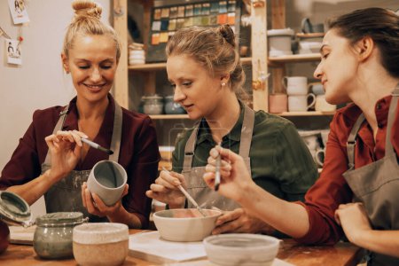 Une entreprise de trois jeunes amies joyeux peignent des céramiques dans un atelier de poterie.