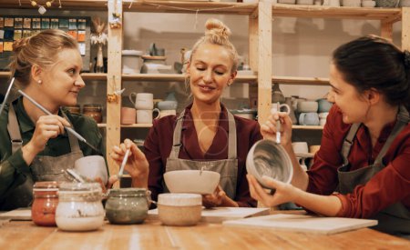 Une entreprise de trois jeunes amies joyeux peignent des céramiques dans un atelier de poterie.