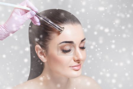 Photo for The cosmetologist makes the procedure Microdermabrasion of the facial skin of a beautiful, young woman in a beauty salon.Cosmetology and New Year's concept. - Royalty Free Image