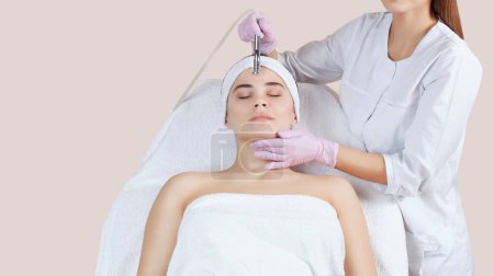 Téléchargez les photos : Le cosmétologue effectue la procédure Microdermabrasion de la peau faciale d'une belle jeune femme dans un salon de beauté.. - en image libre de droit
