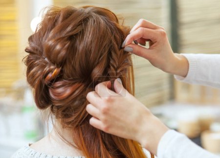 Schöne, rothaarige Mädchen mit langen Haaren, Friseur webt einen französischen Zopf, in einem Schönheitssalon. Professionelle Haarpflege und Frisurengestaltung.