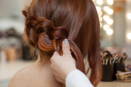 Photo for Beautiful, with long, red-haired hairy girl, hairdresser weaves a French braid, close-up in a beauty salon. Professional hair care and creating hairstyles. - Royalty Free Image