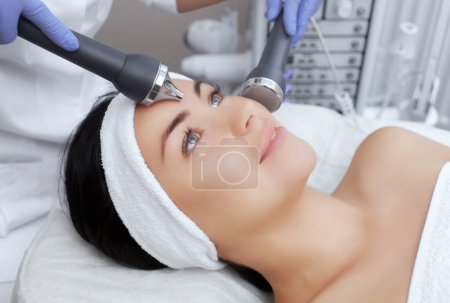 Photo for The cosmetologist makes the procedure an ultrasonic cleaning of the facial skin of a beautiful, young woman in a beauty salon.Cosmetology and professional skin care. - Royalty Free Image