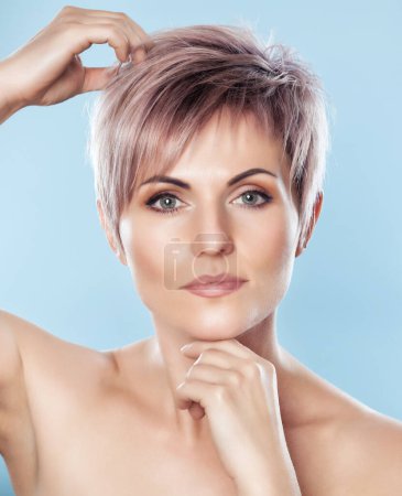 Téléchargez les photos : Portrait of a beautiful blonde woman with beautiful make-up and short haircut after dyeing hair in a hairdressing salon on a blue background. - en image libre de droit