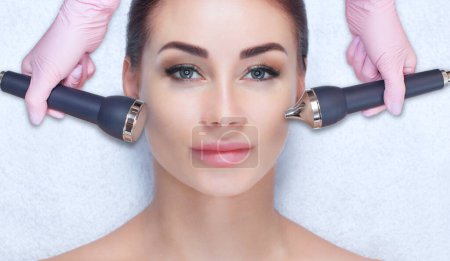 Photo for The cosmetologist makes the ultrasonic cleaning procedure of the facial skin of a beautiful woman in a beauty salon.Cosmetology and professional skin care. - Royalty Free Image
