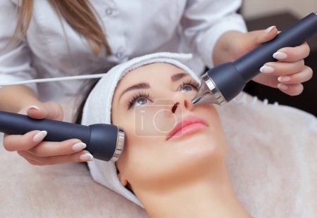 The cosmetologist makes the procedure an ultrasonic cleaning of the facial skin of a beautiful, young woman in a beauty salon.Cosmetology and professional skin care.