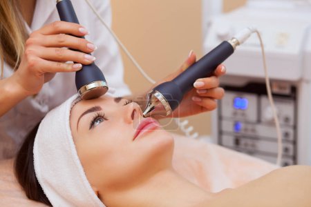 Photo for The doctor-cosmetologist makes the procedure an ultrasonic cleaning of the facial skin of a beautiful, young woman in a beauty salon.Cosmetology and professional skin care. - Royalty Free Image