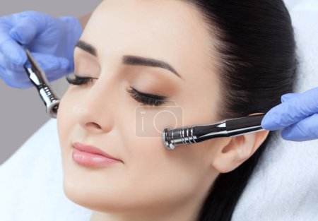 Photo for The cosmetologist makes the Microdermabrasion procedure of the facial skin of a beautiful, young woman in a beauty salon.Cosmetology and professional skin care. - Royalty Free Image