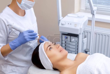 Téléchargez les photos : Le cosmétologue effectue la procédure Thérapie microactuelle de la peau faciale d'une belle jeune femme dans un salon de beauté.. - en image libre de droit