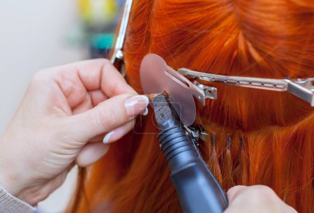 Téléchargez les photos : Le coiffeur fait des extensions de cheveux à une jeune fille rousse, dans un salon de beauté. Soins capillaires professionnels
. - en image libre de droit