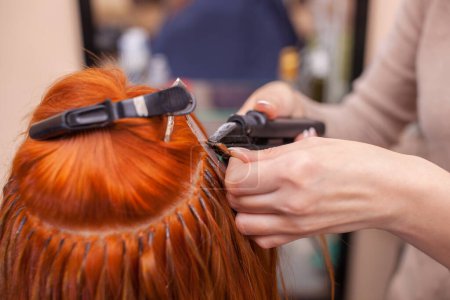 Téléchargez les photos : Le coiffeur fait des extensions de cheveux à une jeune fille rousse, dans un salon de beauté. Soins capillaires professionnels
. - en image libre de droit