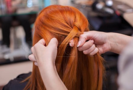 Photo for Beautiful red-haired girl, hairdresser weave a French braid close-up, in a beauty salon. Professional hair care and creating hairstyles. - Royalty Free Image