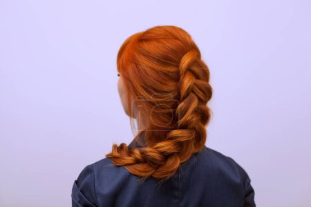 Foto de Hermosa chica de pelo largo y rojo, trenzada con una trenza francesa, en un salón de belleza. Cuidado profesional del cabello y la creación de peinados. - Imagen libre de derechos