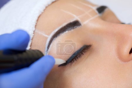 Maquillage permanent pour les sourcils de belle femme aux sourcils épais dans un salon de beauté. Esthéticienne en gros plan faisant tatouer les sourcils.
