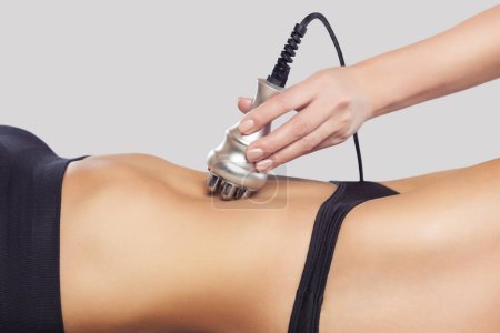 The doctor does the Rf lifting procedure on the abdomen and hips of a woman in a beauty parlor. Treatment of overweight and flabby skin.