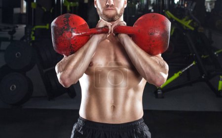 Foto de Muscular hombre levanta una pesada kettlebell durante un entrenamiento en el gimnasio. Concepto deportivo, quema de grasa y estilo de vida saludable. - Imagen libre de derechos