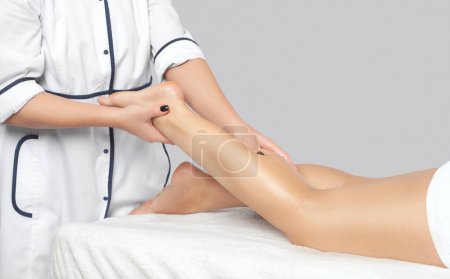 Foto de Un médico ortopédico hace masaje del pie y la parte inferior de la pierna del paciente después de una lesión en la clínica.Concepto de cosmetología y masaje.Concepto de cosmetología y masaje. - Imagen libre de derechos