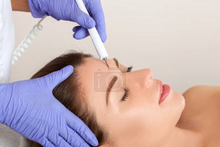 Photo for The doctor-cosmetologist makes the procedure treatment of Couperose of the facial skin of a beautiful, young woman in a beauty salon.Cosmetology and professional skin care. - Royalty Free Image