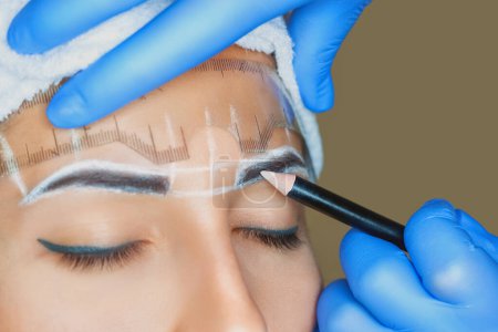 Téléchargez les photos : Permanent make-up for eyebrows of beautiful woman with thick brows in beauty salon. Closeup beautician doing tattooing eyebrow. Professional makeup and cosmetology skin care. - en image libre de droit