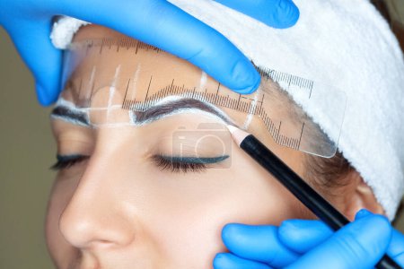 Téléchargez les photos : Permanent make-up for eyebrows of beautiful woman with thick brows in beauty salon. Closeup beautician doing tattooing eyebrow. Professional makeup and cosmetology skin care. - en image libre de droit
