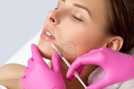 Frau mit schöner, sauberer Haut. Kosmetologe führt Injektionen an den Lippen und in die Nasolabialfalten einer schönen Frau durch. Kosmetik für Frauen im Schönheitssalon.