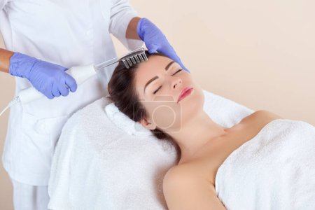 Téléchargez les photos : Le cosmétologue fait la thérapie Microcurrent contre la perte de cheveux sur les cheveux dans un salon de beauté. Cosmétologie et soins professionnels de la peau. - en image libre de droit