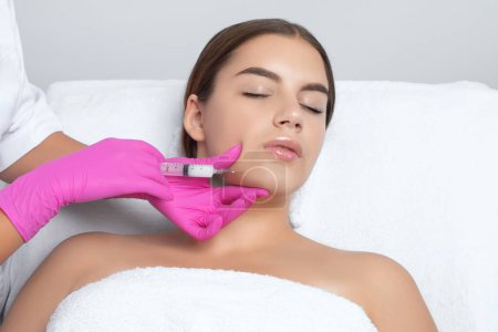 Cosmetologist makes lipolytic injections to burn fat on the chin, cheeks and neck of a woman against double chin. Female aesthetic cosmetology in a beauty salon.Cosmetology concept.