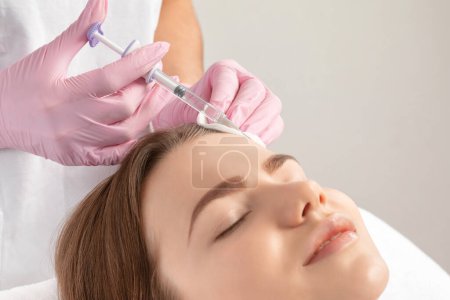 Foto de El cosmetólogo hace rejuvenecedoras inyecciones antiarrugas en la cara de una mujer hermosa. Cosmetología estética femenina en un salón de belleza. - Imagen libre de derechos