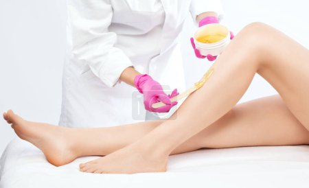 Foto de Una esteticista hace una depilación de las piernas de una mujer en un salón de belleza. Cosmetología estética femenina. - Imagen libre de derechos