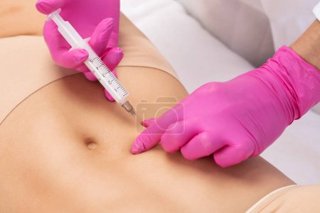 doctor of aesthetic cosmetology makes lipolytic injections to burn body fat on a womans stomach and body.Female aesthetic cosmetology in beauty salon.