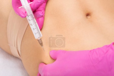 médico de cosmetología estética hace inyecciones lipolíticas para quemar la grasa corporal en un estómago y el cuerpo de las mujeres. Cosmetología estética femenina en un salón de belleza.