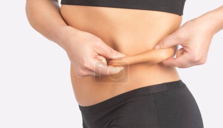 Photo for Girl pulls the skin on the abdomen, showing the body fat in the abdominal area and sides. Treatment and disposal of excess weight, the deposition of subcutaneous fat. - Royalty Free Image