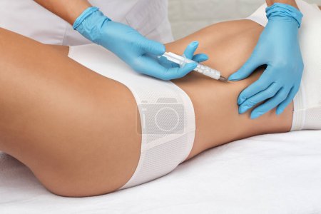 cosmetologist makes lipolytic injections to burn fat on the stomach and waist of a woman. Female aesthetic cosmetology in a beauty salon.Cosmetology concept.