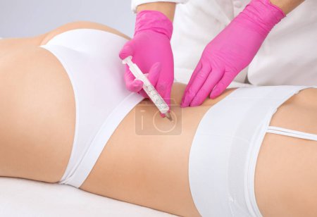 Kosmetikerin macht lipolytische Injektionen, um einer Frau Fett auf Rücken und Taille zu verbrennen. Weibliche ästhetische Kosmetologie im Schönheitssalon. Kosmetologie-Konzept.
