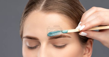 Makeup artist does facial hair removal procedure. Beautiful girl with blue eyes having Permanent Make-up on her Eyebrows.  Professional makeup.